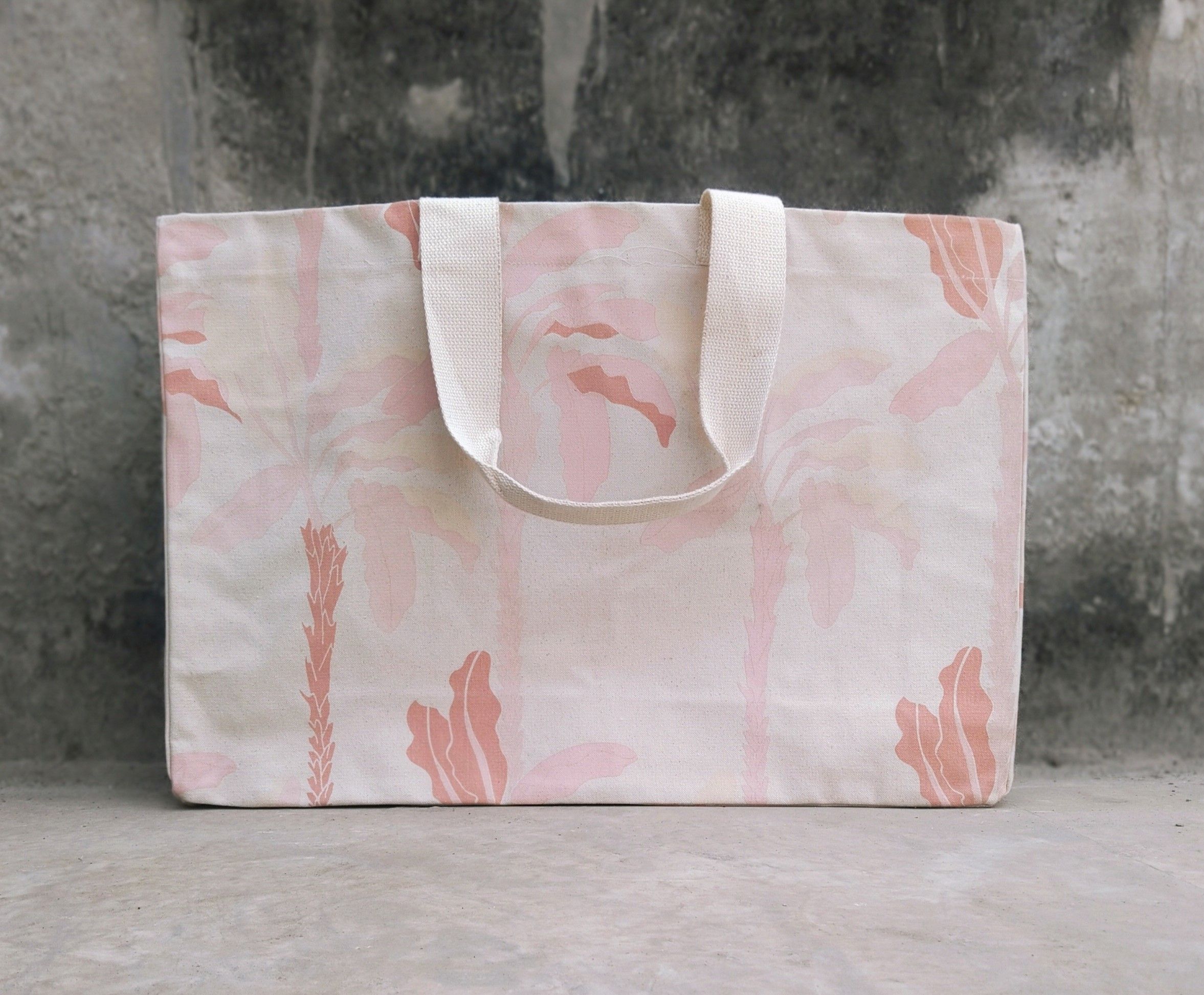 Pink and cream tote bag with leaf pattern on concrete surface.