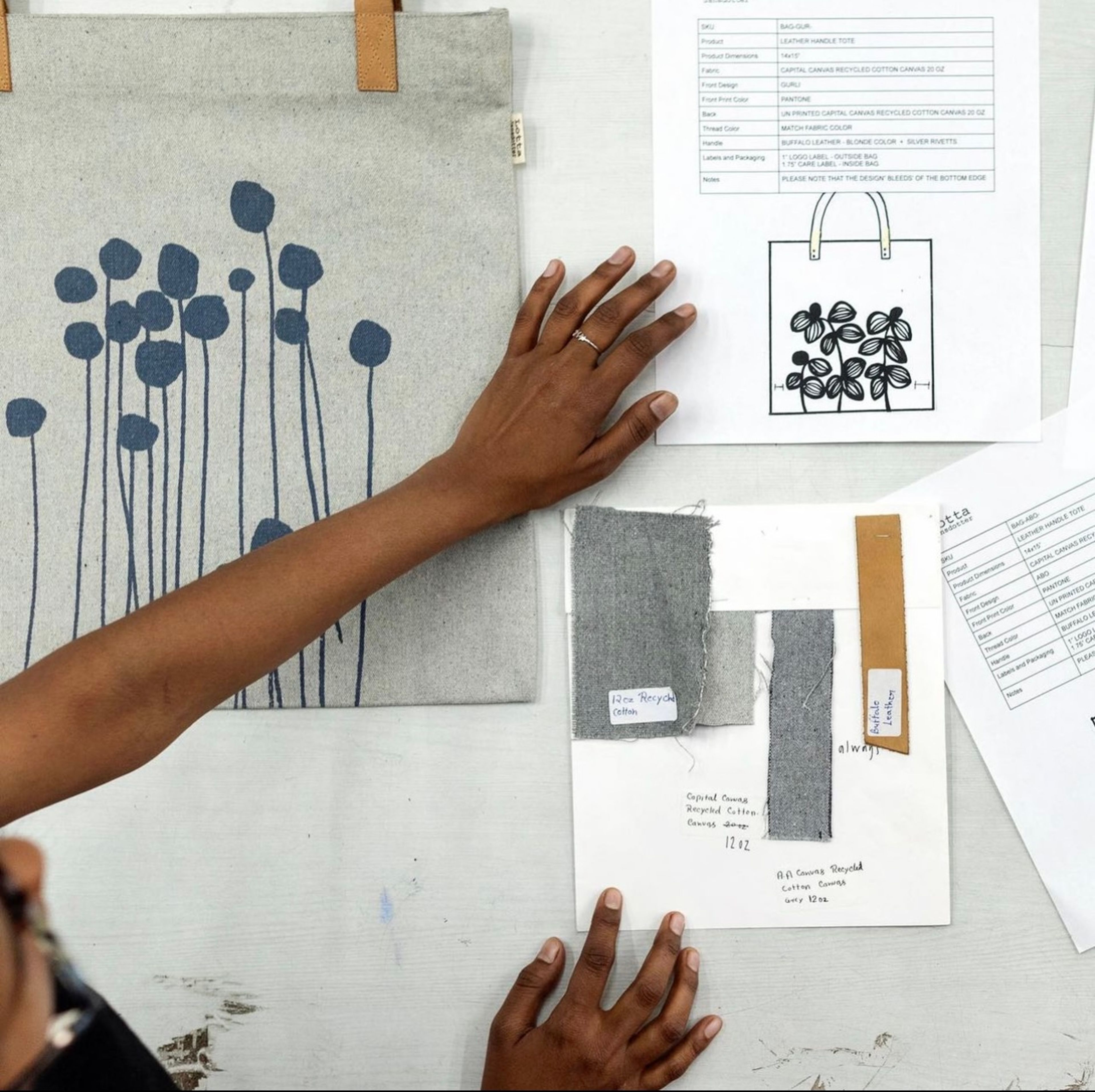Designer reviewing leather tote bag prototype with botanical print and fabric samples.
