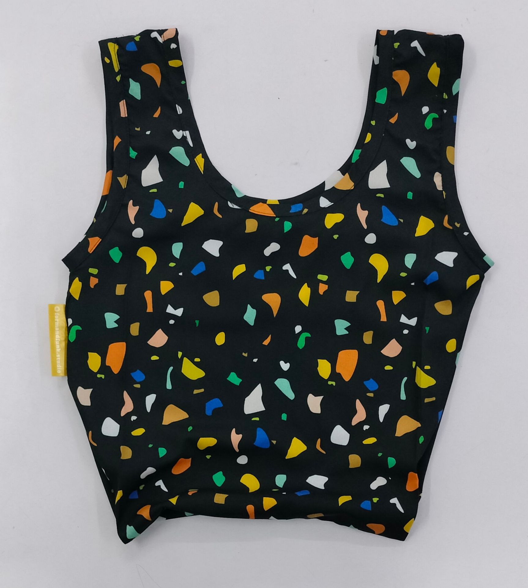 Black sleeveless crop top with colorful geometric pattern scattered throughout.
