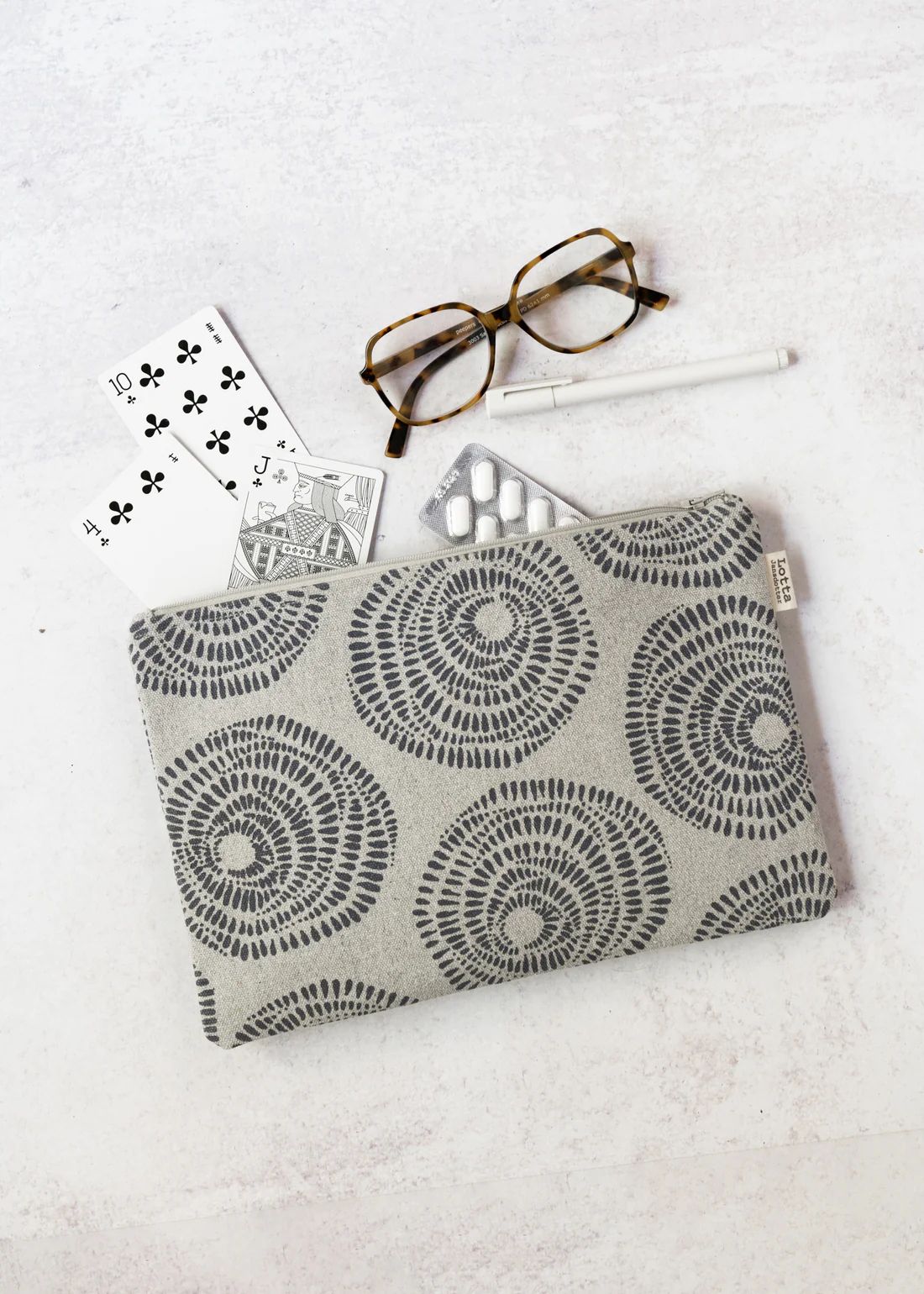 Patterned pouch with glasses, playing cards, pen, and pills on white surface.