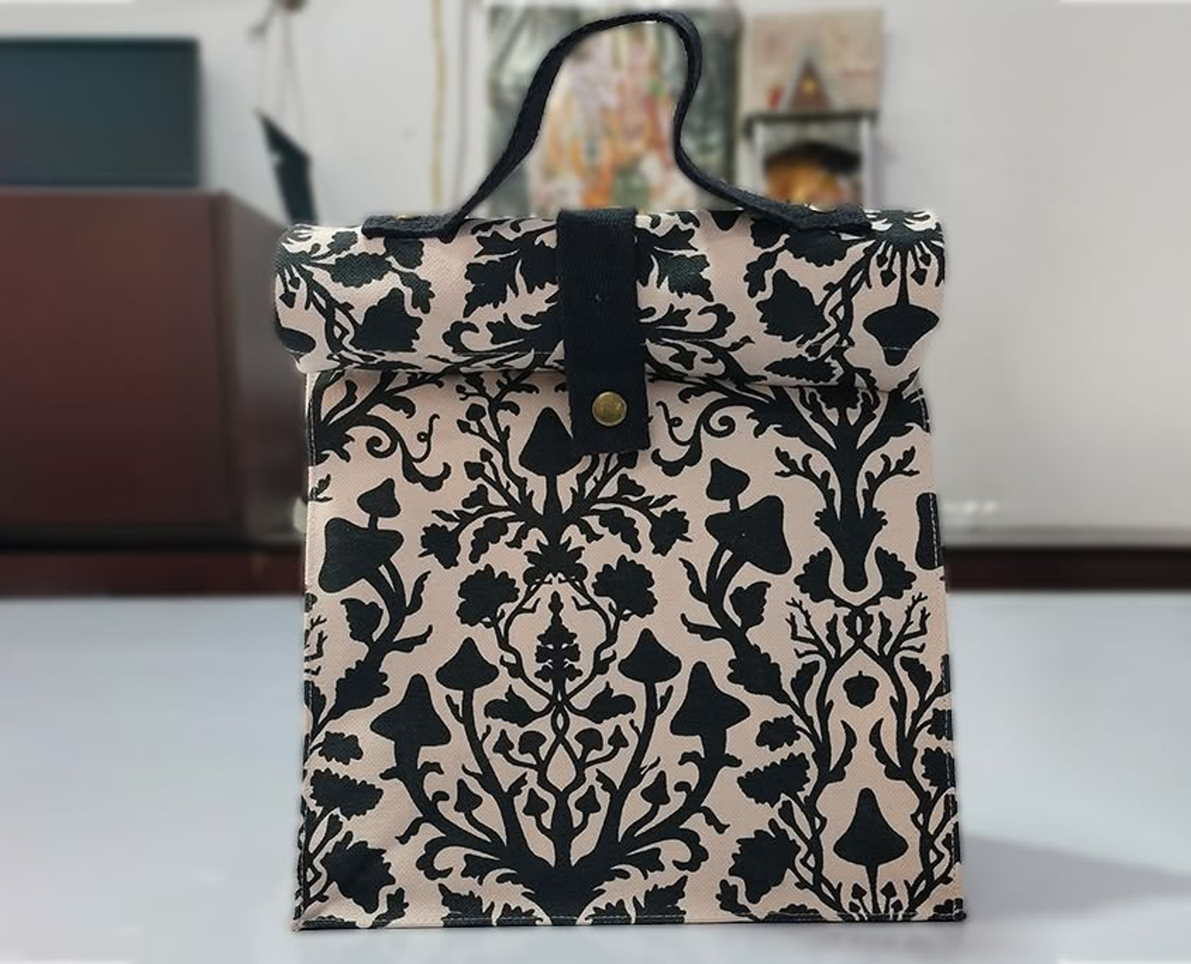 Decorative fabric bag with black botanical damask pattern on cream background, displayed indoors.