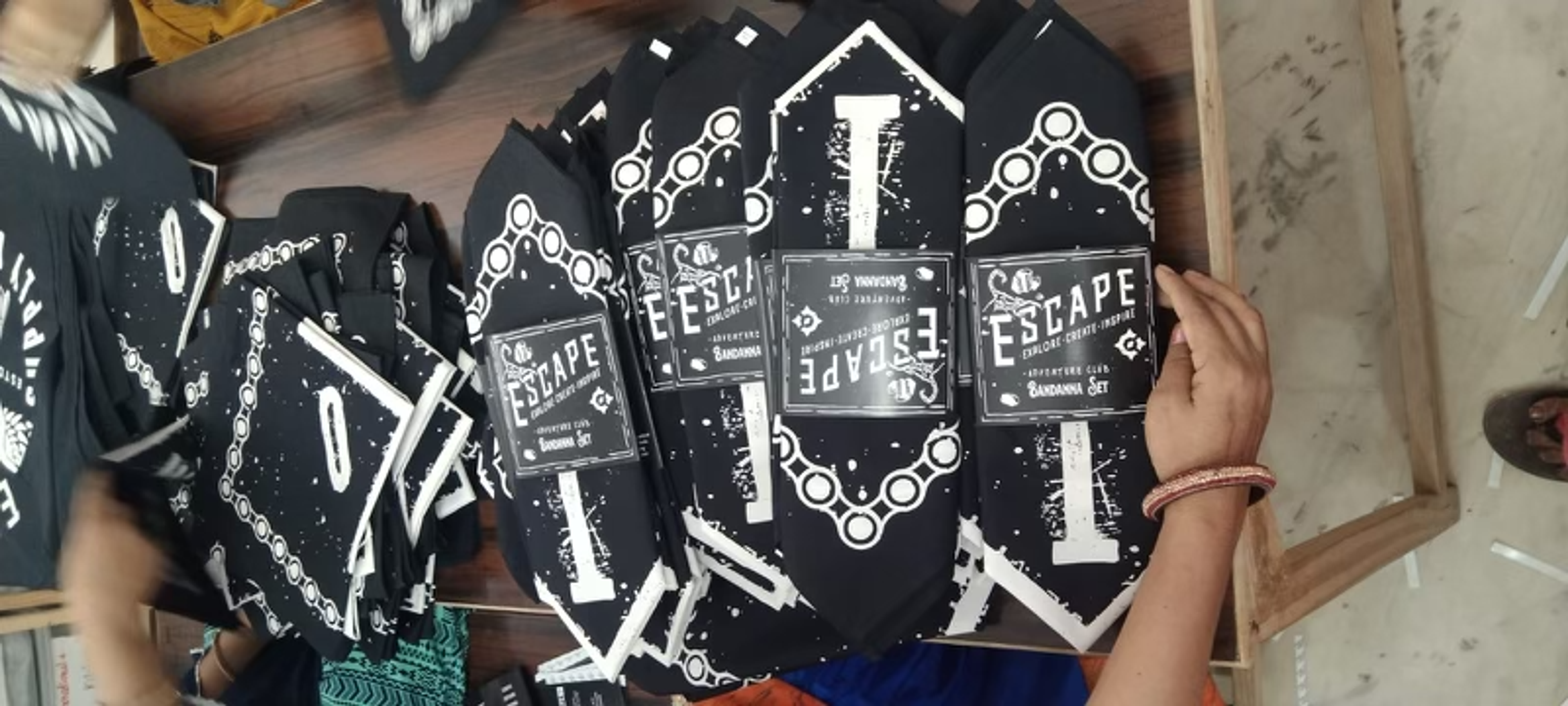 Person holding black "Escape" branded merchandise with white decorative designs and text.