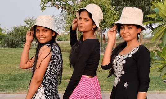 Three women wearing matching cream bucket hats pose together outdoors in a park setting.