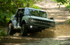 Green Ford Bronco driving through a mud puddle