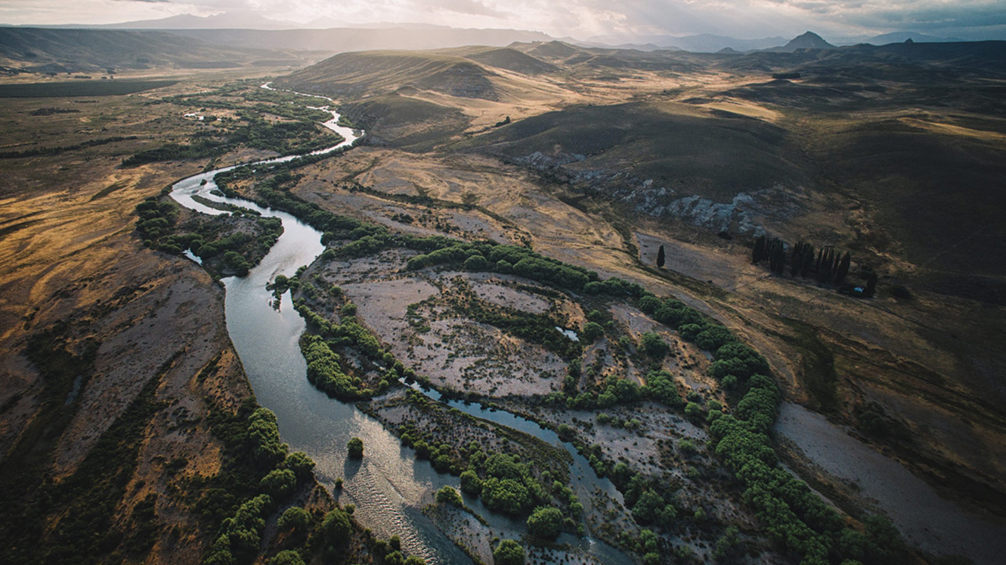 Landscape of a rugged, high plains terrain with few green trees and a winding river.