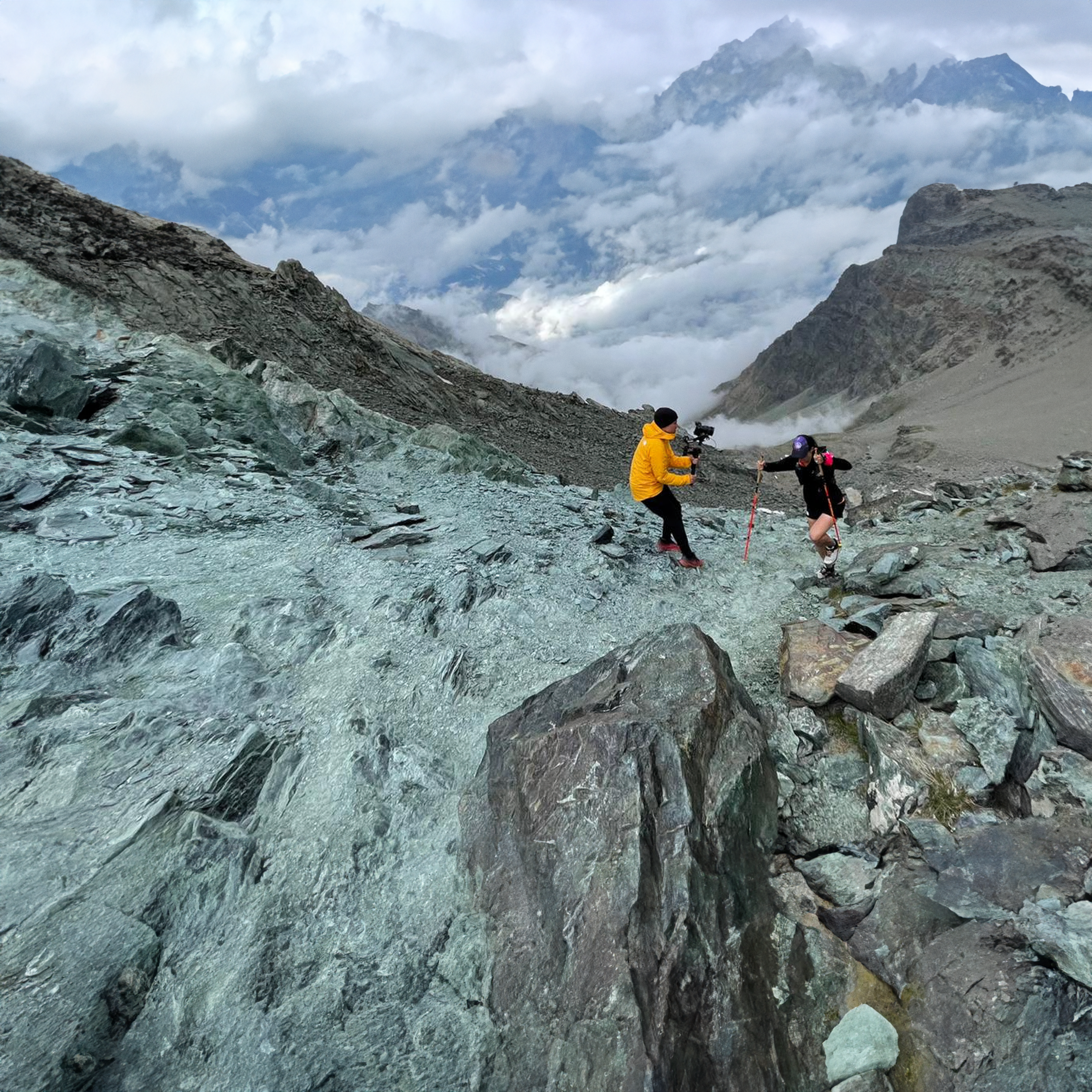 A climber with poles being filmed on a mountain pass
