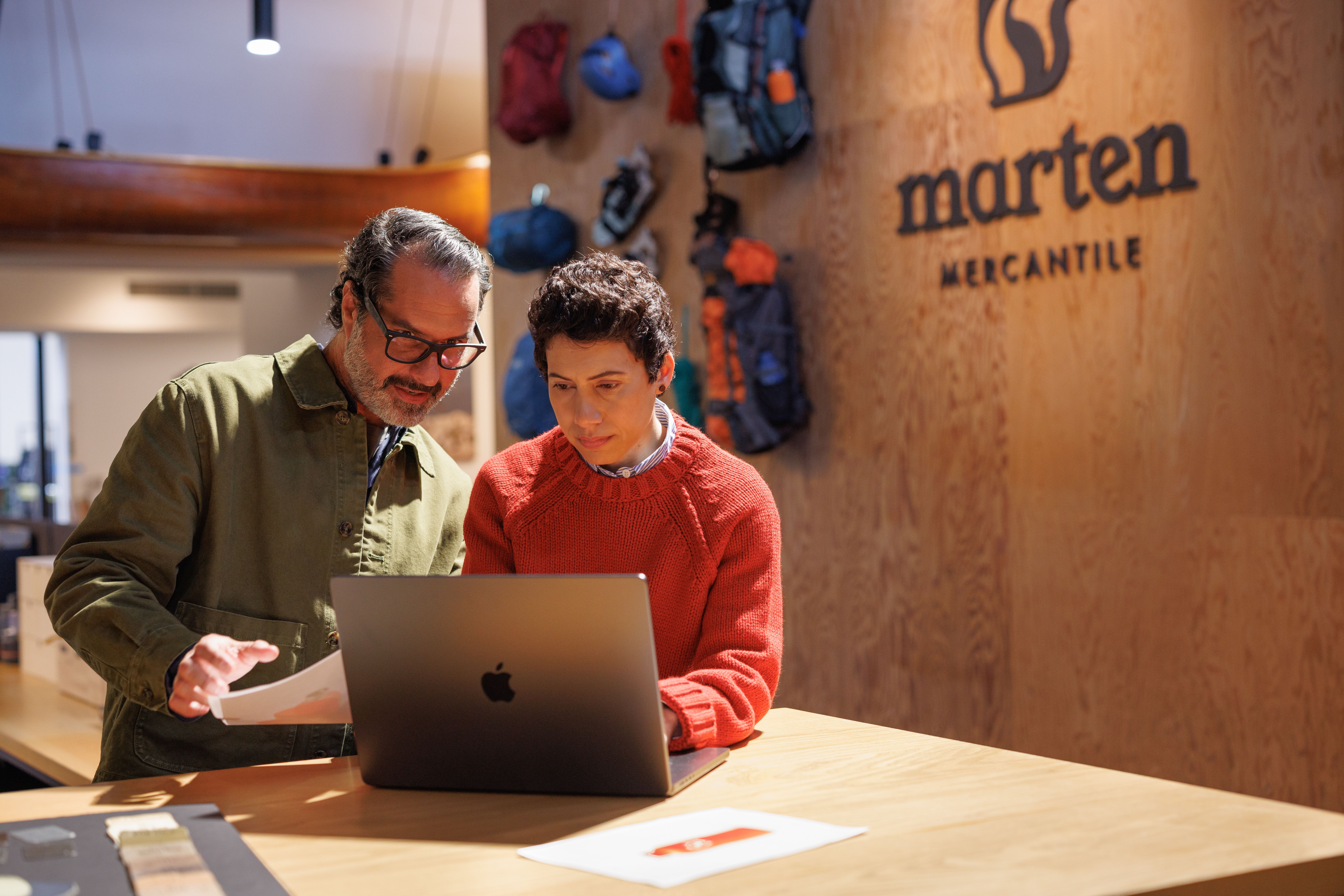 Two people looking at a laptop at a wooden counter in a store with the "Marten Mercantile" logo.