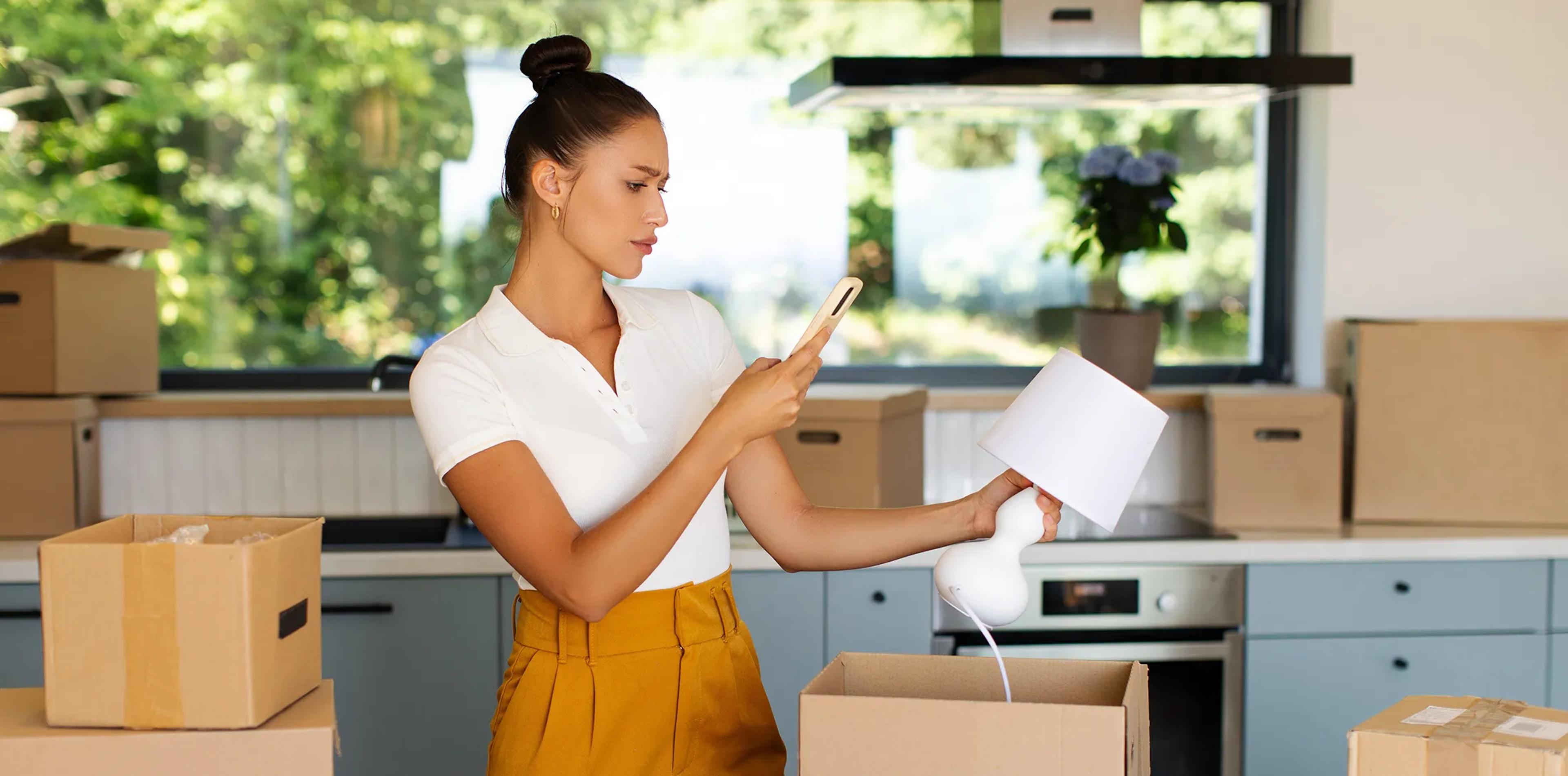 A woman photographing a lamp with her phone while packing household belongings
