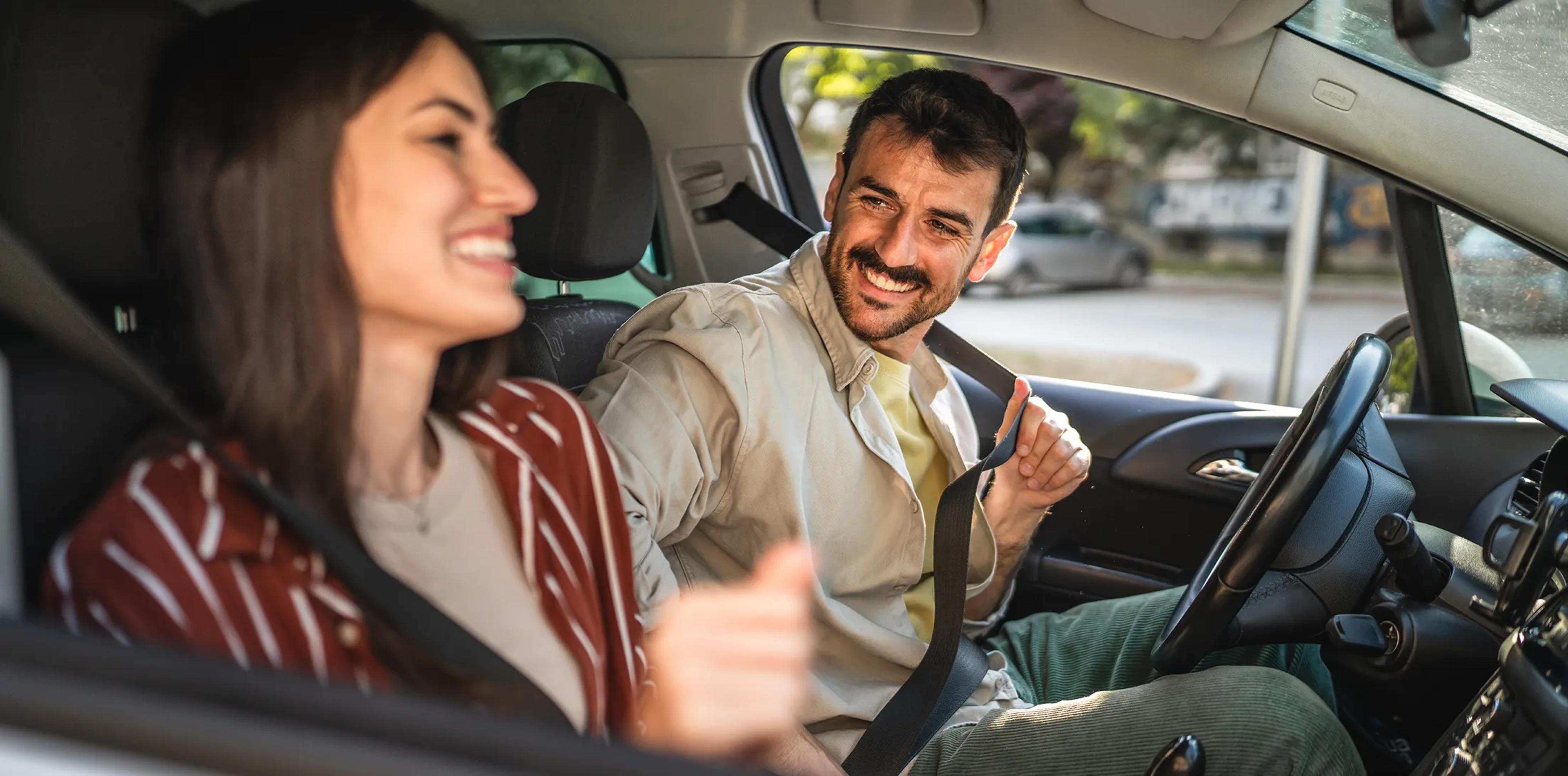 Two adults fastening their seat belts in a car