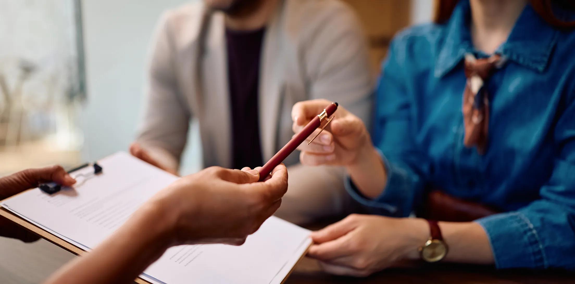 An advisor handing a pen to clients as they review paperwork