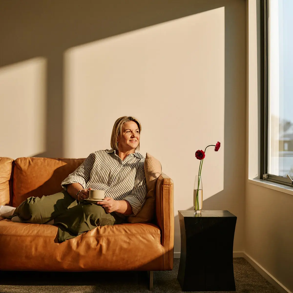 Woman with coffee at a window in a sunlight room.