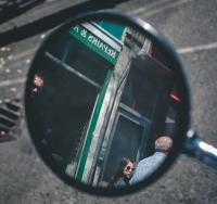 A girl in sunglasses is looking over her shoulder seen reflected in a moped mirror.