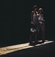 Two ladies walk through a shaft of light with the rest of the frame in darkness.