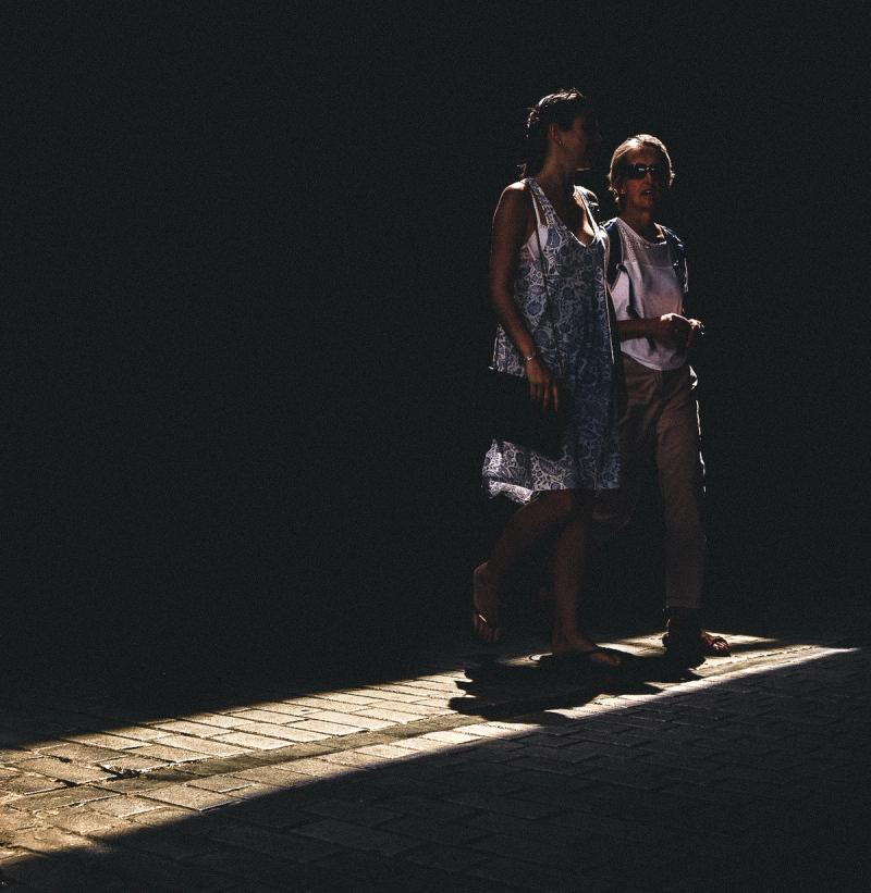 Two ladies walk through a shaft of light with the rest of the frame in darkness.