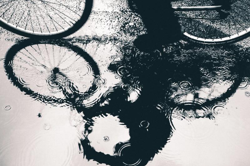 A reflection of a bicycle seen in a puddle with a lot of ripples. Black and white. 