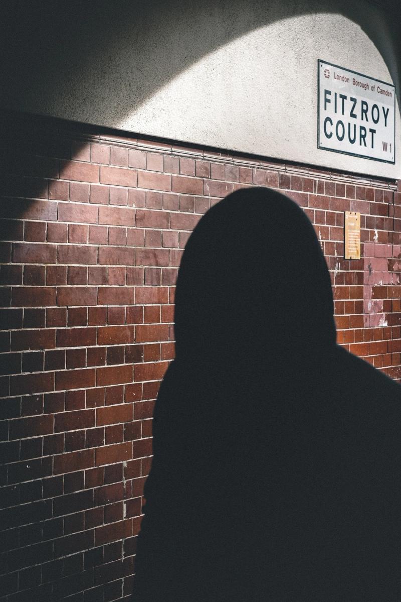 A silhouette of a person in a oval beam of light with a street sign for 'FITZROY COURT' visible behind them.