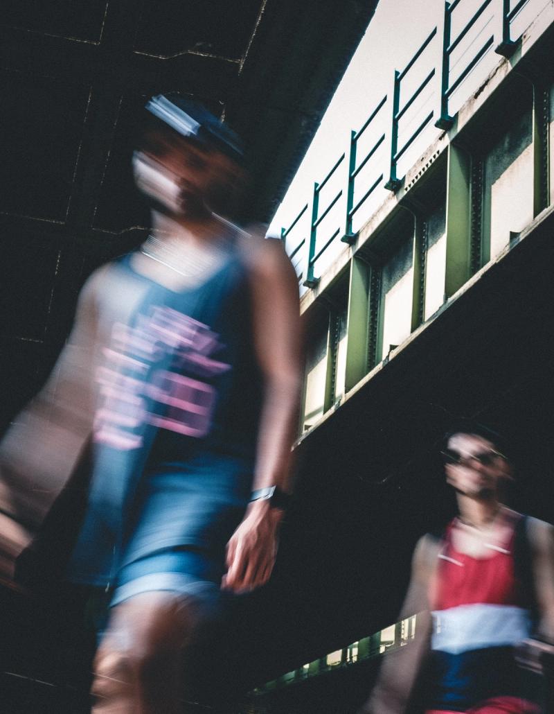 Two blurred figures of young men seen from a low angle walking under a bridge.