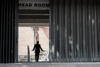 the silhouette of a man with his hands out to the side, between some metal shutter gates three times his size, with the words HEAD ROOM visible above his head.