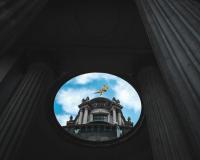 An old London building with a gold angel on the to seen through a hole in another old building in the foreground. It looks a bit like a renaissance painting in an oval frame.