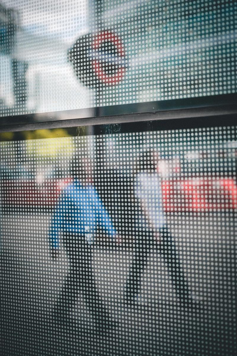 Two people are walking in step with an underground roundel behind them. The scene is viewed through glass covered in small round dots at regular intervals giving the appearance of a low-resolution scan.