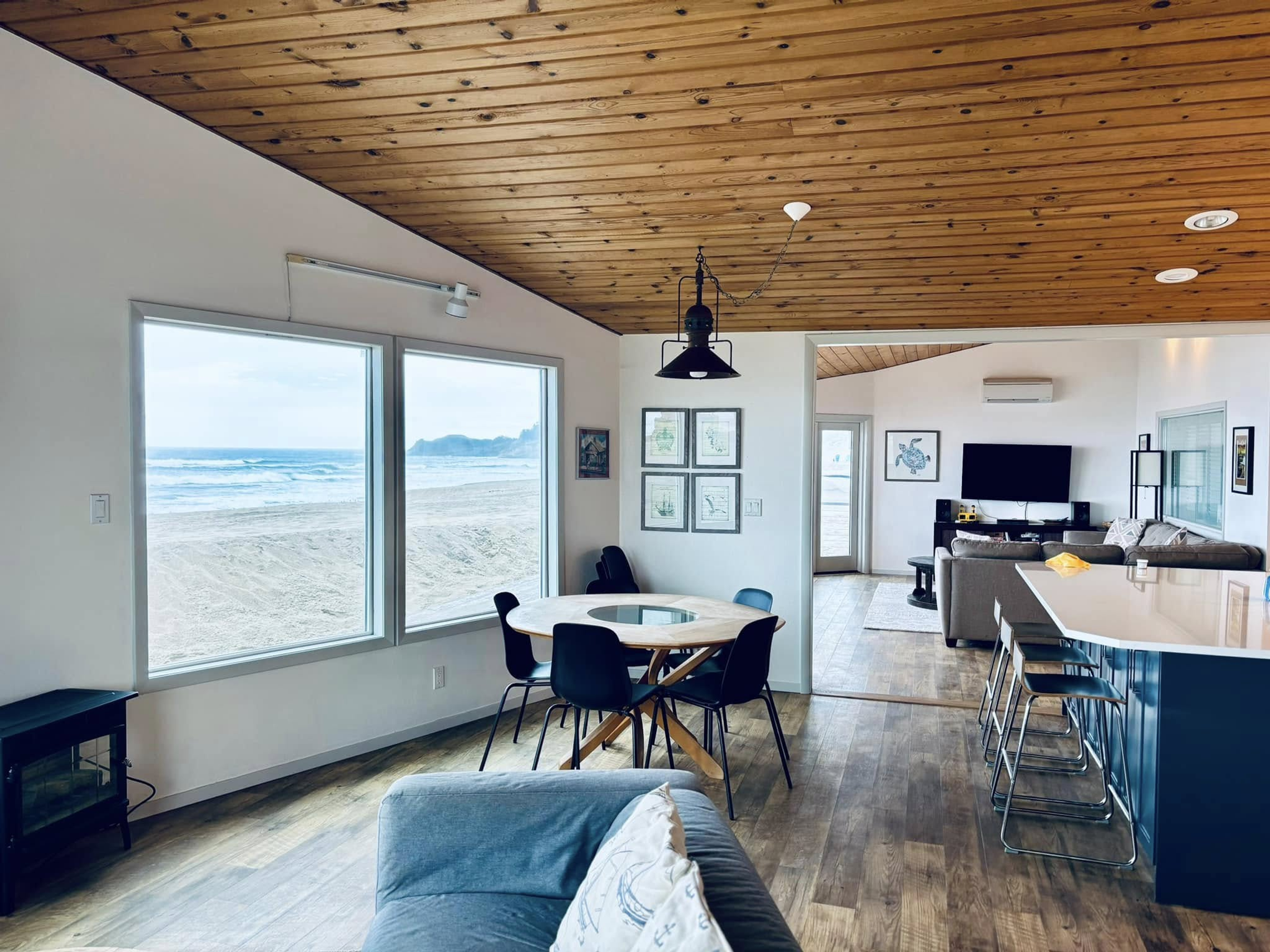 Open living room and kitchen with a wood ceiling and windows onto a beach
