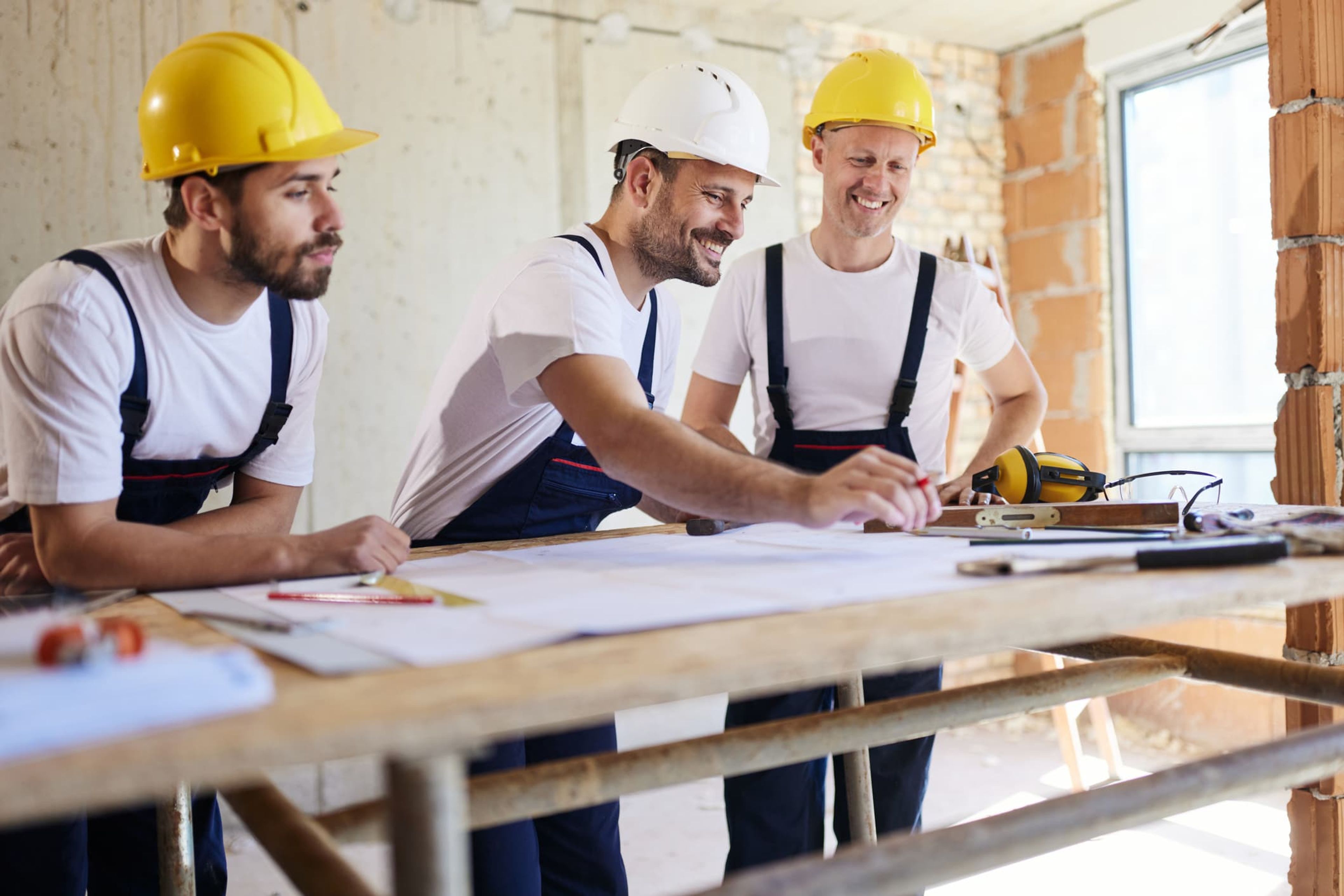 Three builders in hard hats reviewing plans on a job site