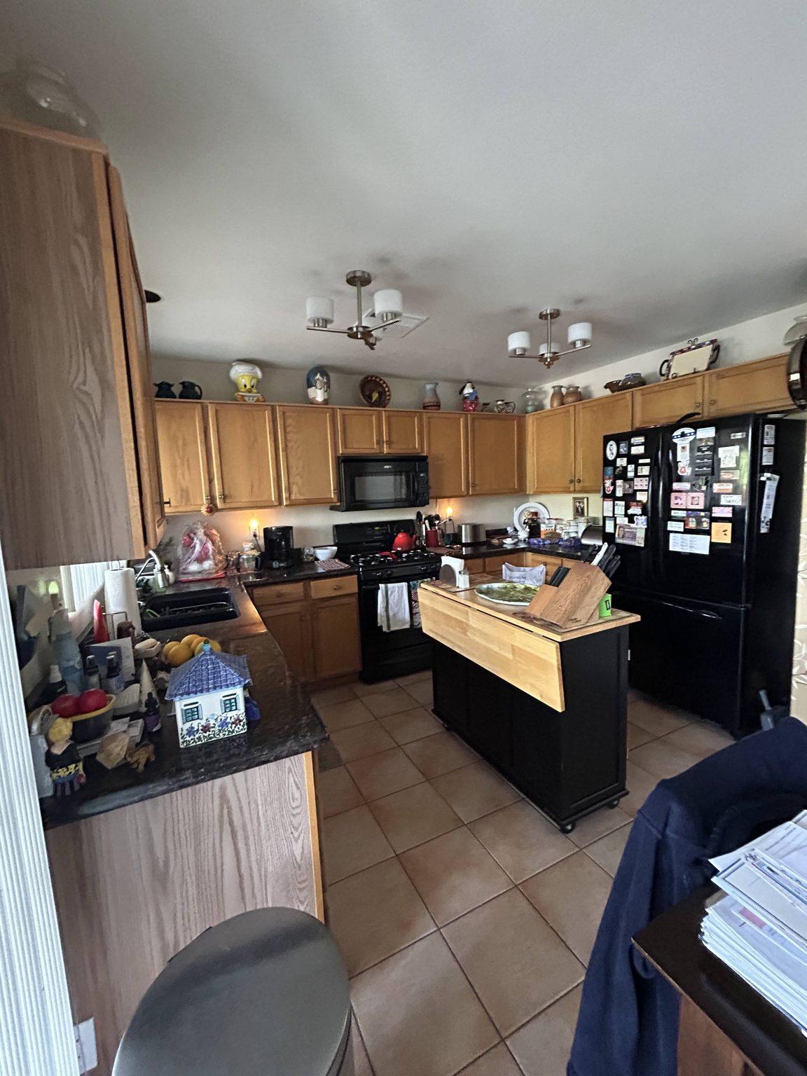 Before the remodel: the original kitchen with honey oak cabinets, black appliances, dark counters and tile floor.