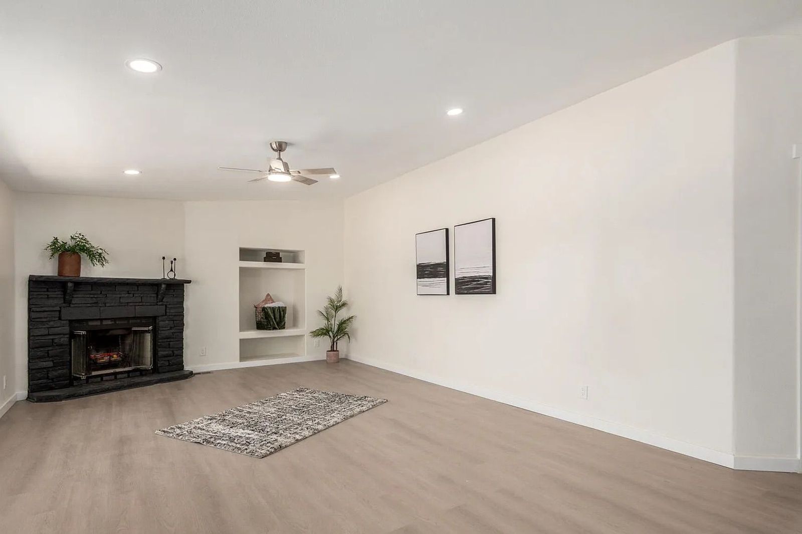 Empty living room featuring light wood-plank flooring, a black painted brick fireplace, and built-in display shelves.