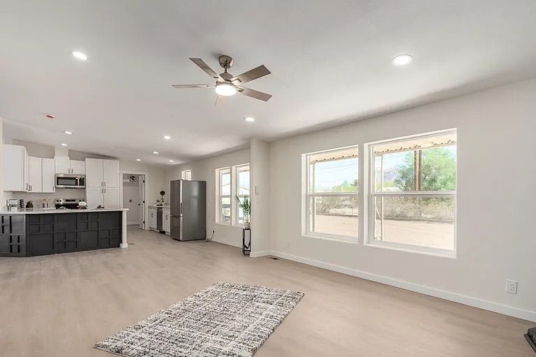 Open concept living and kitchen area featuring light wood flooring, large windows, and a bright kitchen with white cabinets and a dark accent island.