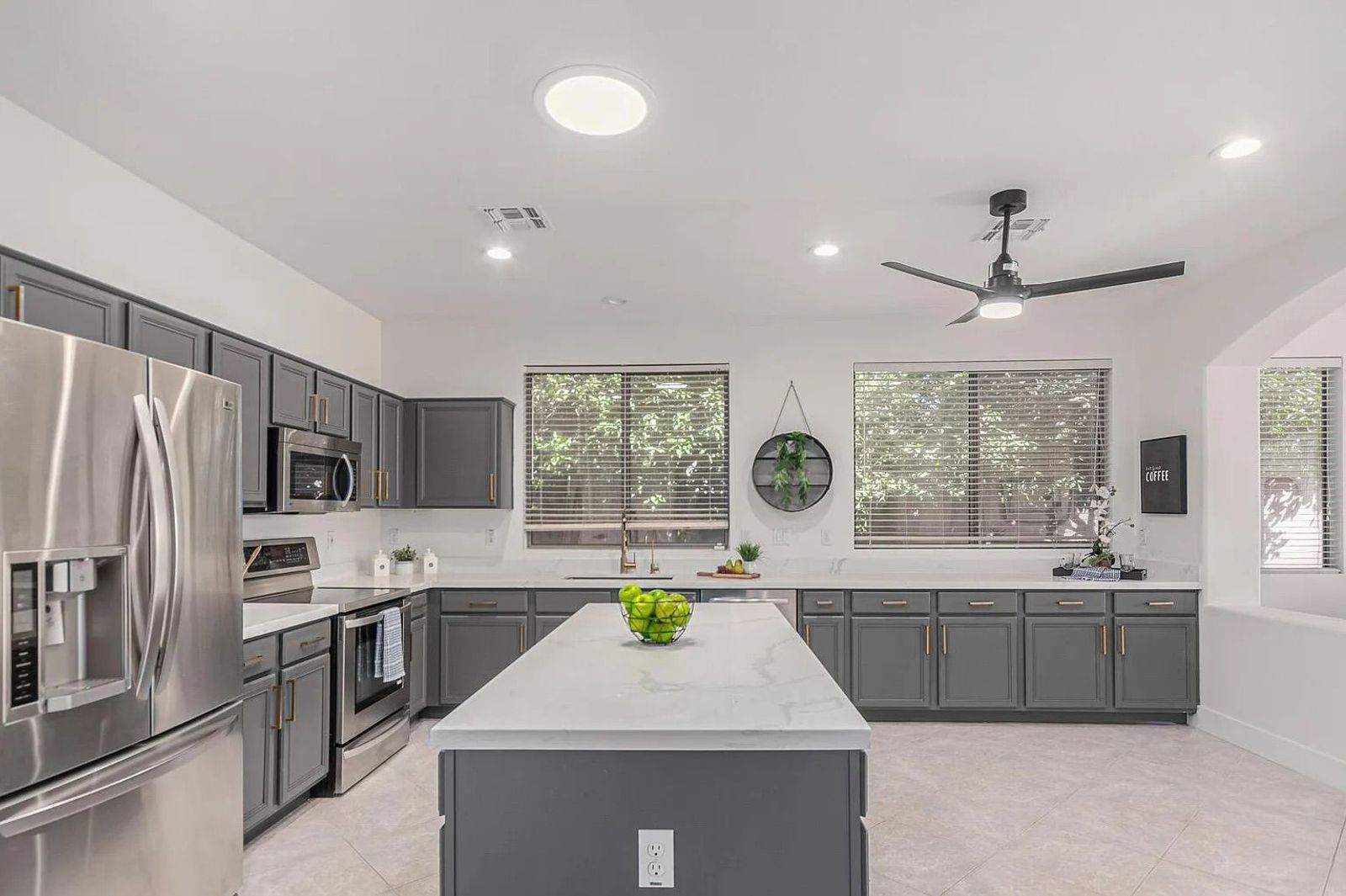 Modern kitchen featuring dark grey cabinetry, white quartz countertops, stainless steel appliances, and a large center island.