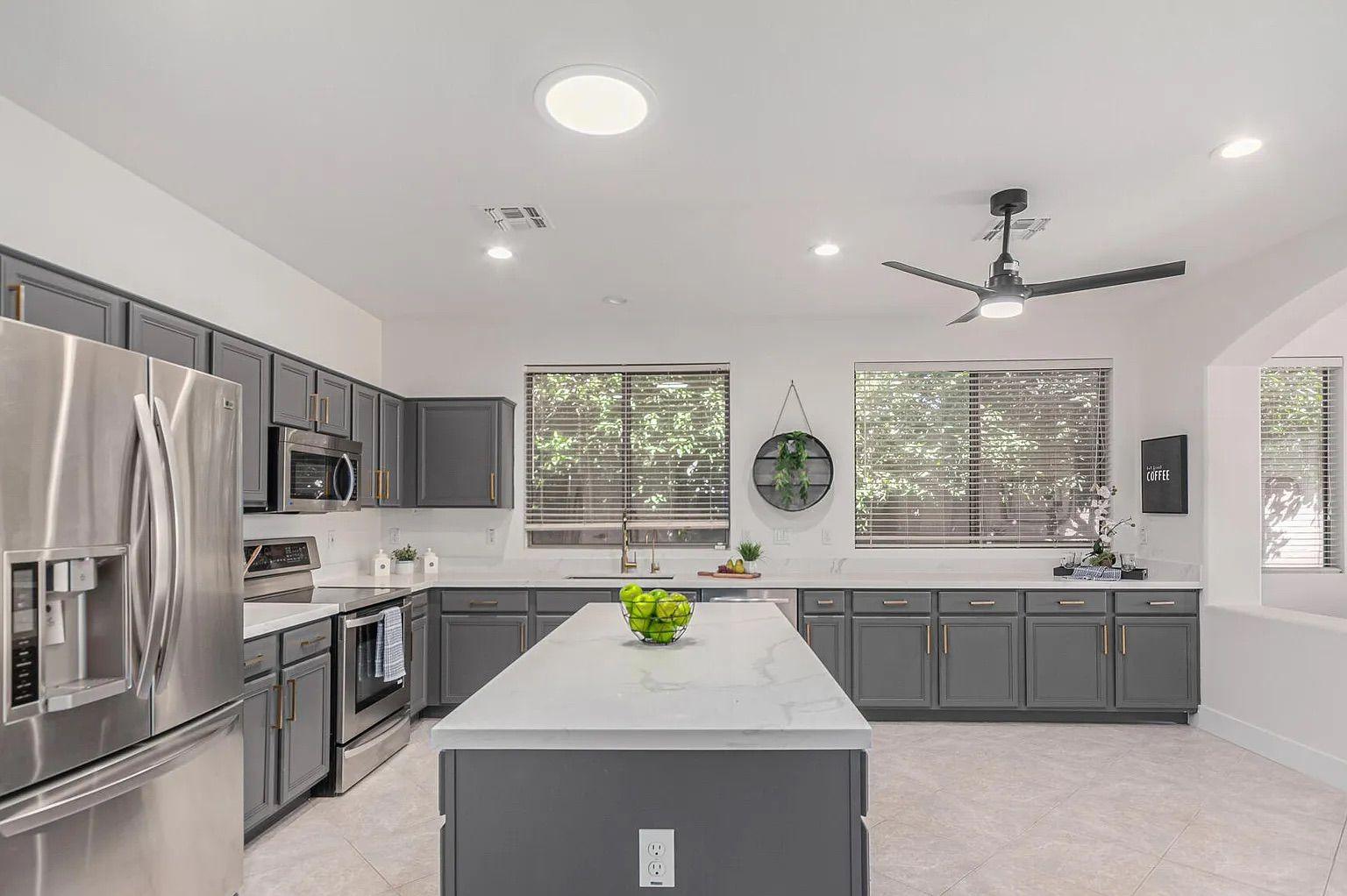 Modern kitchen featuring dark grey cabinetry, white quartz countertops, stainless steel appliances, and a large center island.