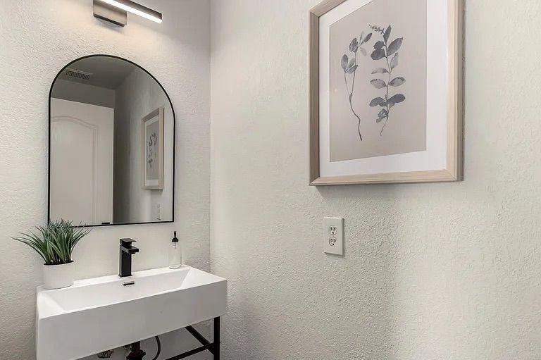 Modern powder room featuring a white trough sink on a black stand, a black-framed arched mirror, and framed botanical wall art.