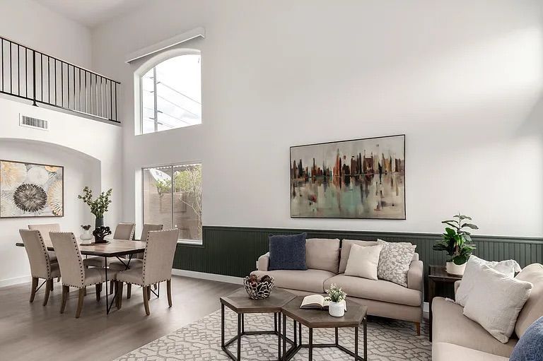 Two-story living room featuring green wainscoting, beige sofas, a dining area, and a second-floor loft balcony overlooking the space.