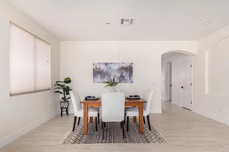 Bright dining area with light tile flooring, a wooden dining table, white upholstered chairs, and abstract wall art.