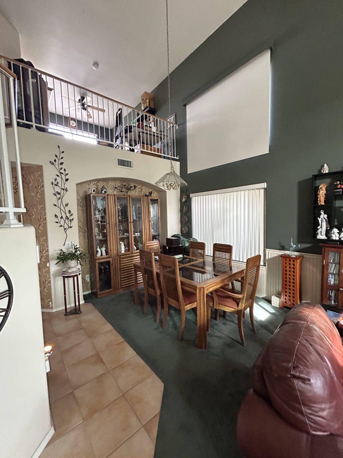 Before the remodel: the original two-story living and dining space with green carpet, tile floor and the loft railing above.