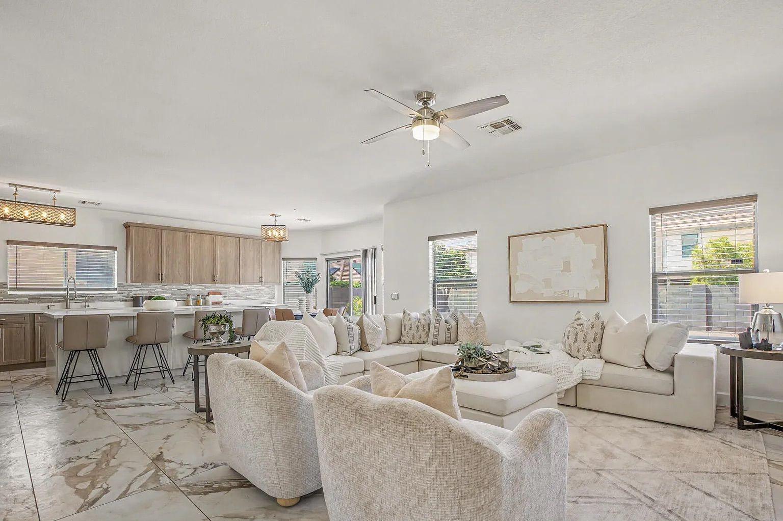 Spacious open-concept living area and kitchen featuring a large white sectional, light wood cabinetry, a large island, and marble-patterned tile flooring throughout.