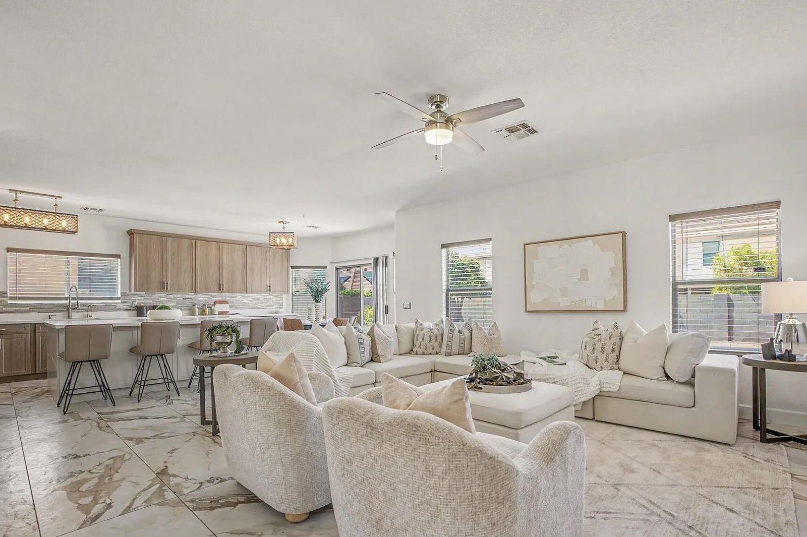 Spacious open-concept living area and kitchen featuring a large white sectional, light wood cabinetry, a large island, and marble-patterned tile flooring throughout.