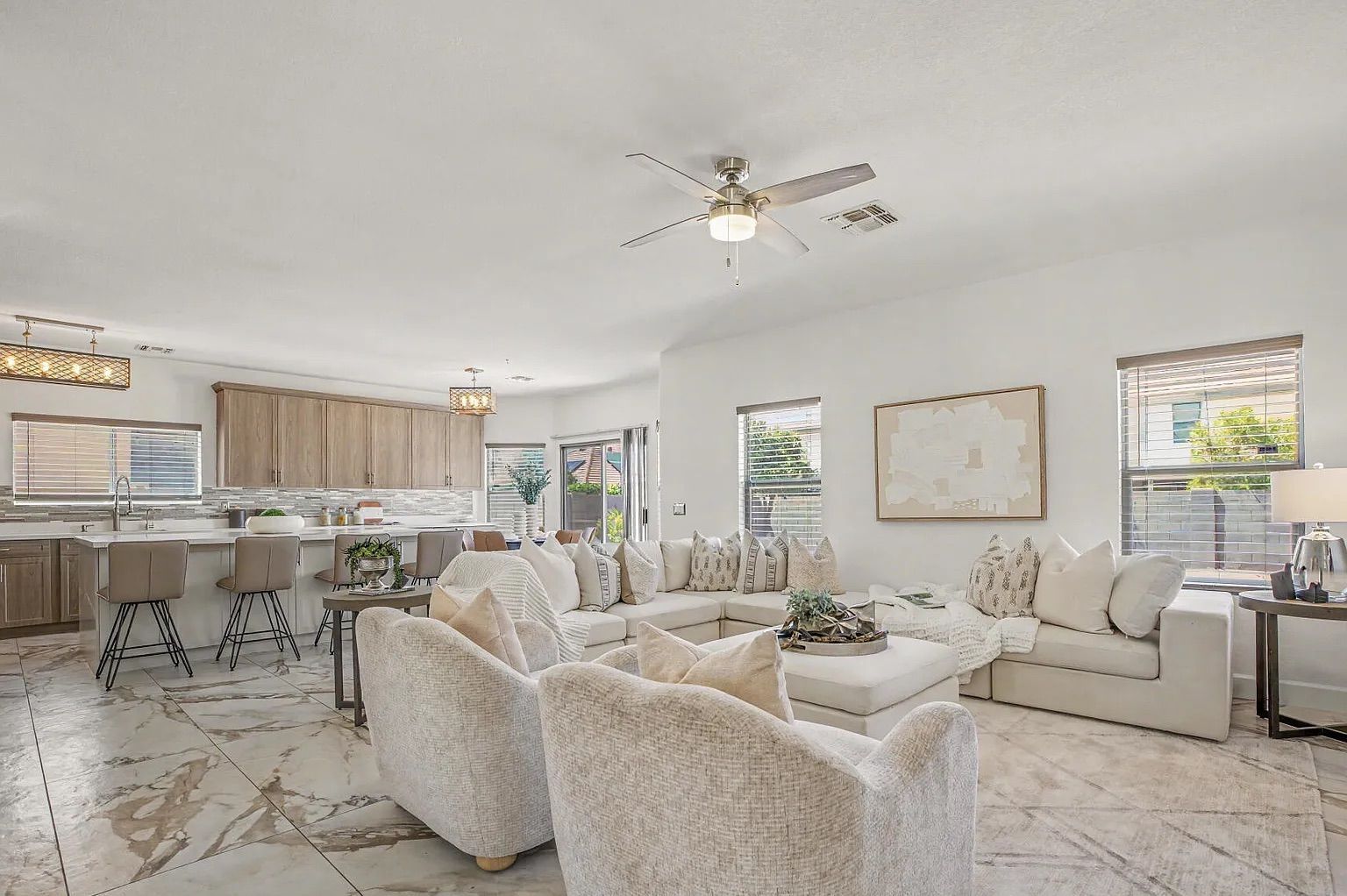 Spacious open-concept living area and kitchen featuring a large white sectional, light wood cabinetry, a large island, and marble-patterned tile flooring throughout.
