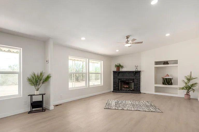 Bright, open living space with large windows, light wood flooring, a black brick corner fireplace, and built-in display shelves.