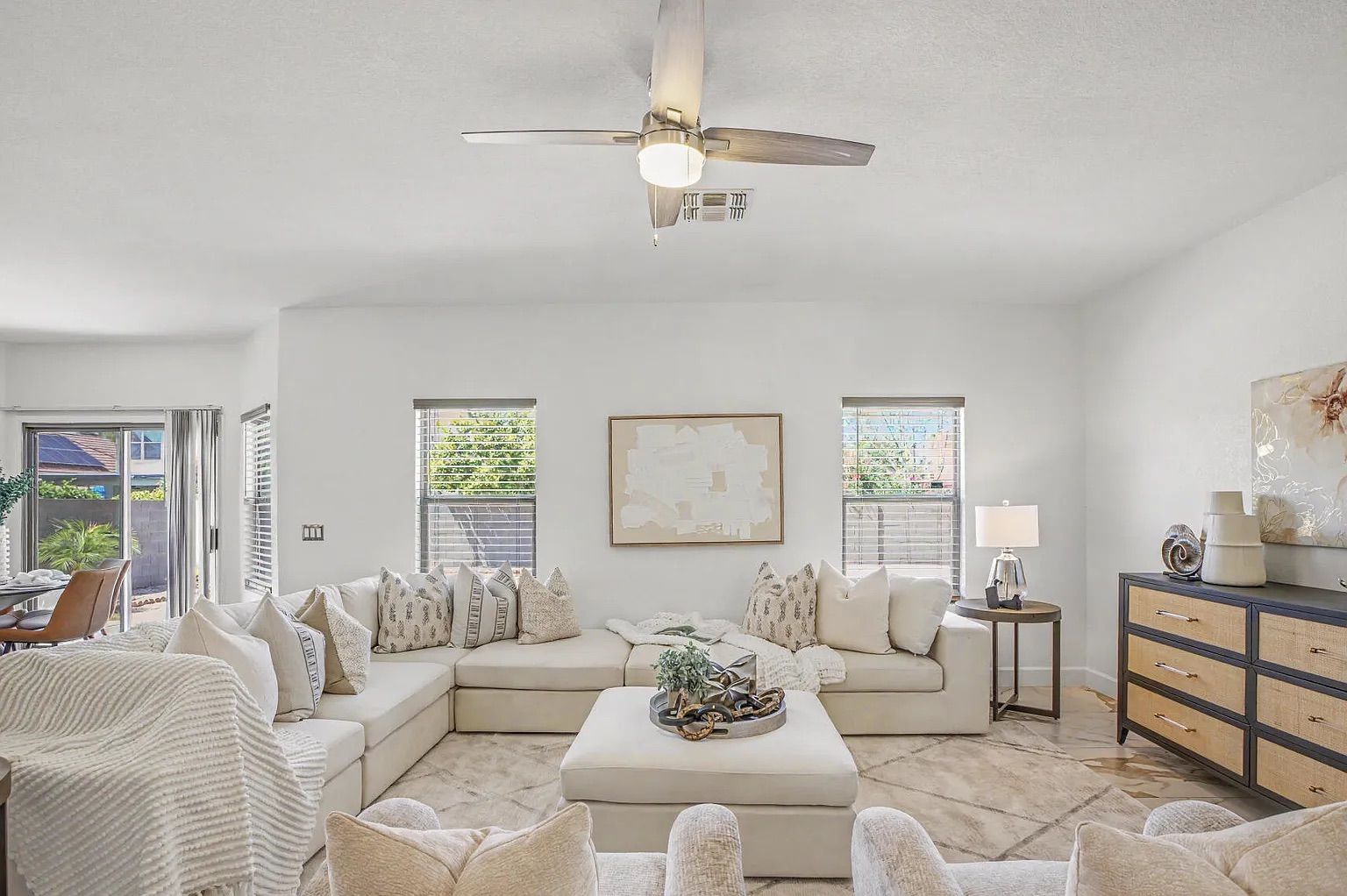 Cozy living room seating area focused on a large white U-shaped sectional sofa, a matching square ottoman, and a wood and cane console table against the wall.