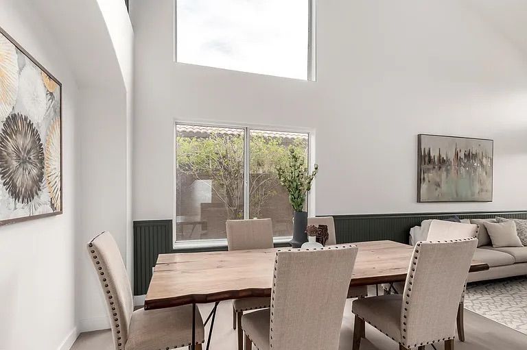 Open concept dining area featuring a rustic wood table with upholstered chairs, situated next to a staircase and adjacent living room.