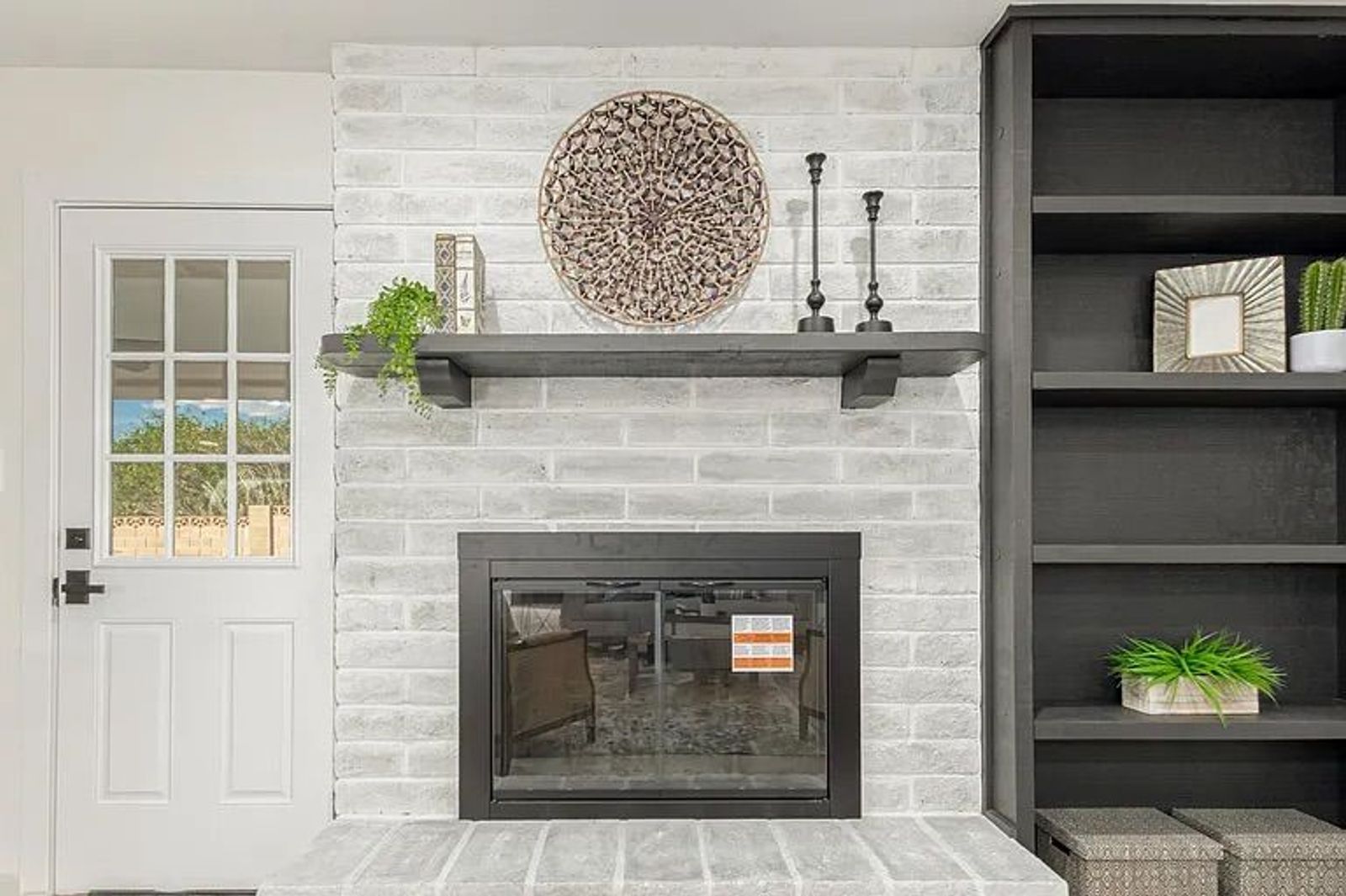 Close-up of a living room fireplace featuring whitewashed brick, a black mantel with decor, a black glass fireplace insert, and adjacent black built-in bookshelves.