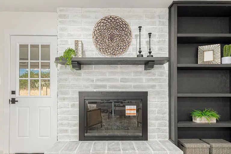 Close-up of a living room fireplace featuring whitewashed brick, a black mantel with decor, a black glass fireplace insert, and adjacent black built-in bookshelves.