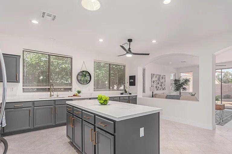 Spacious grey and white kitchen with a large center island, looking out over a half-wall into an open living room area.
