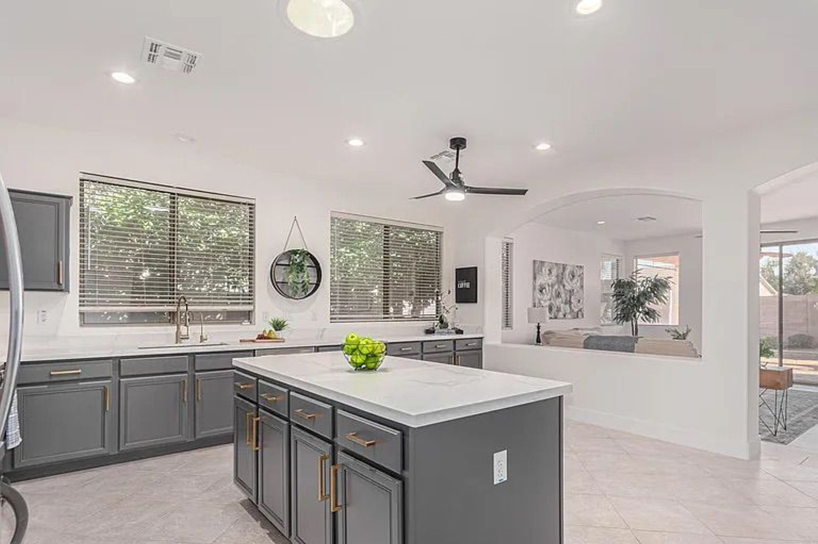 Spacious grey and white kitchen with a large center island, looking out over a half-wall into an open living room area.