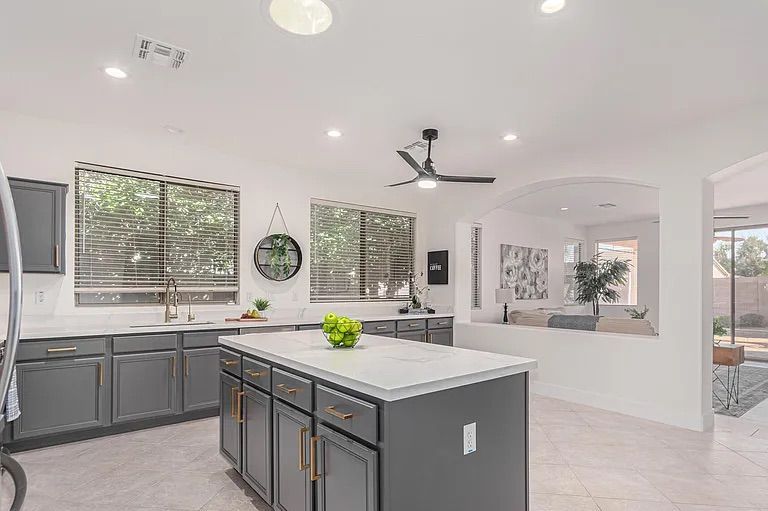 Spacious grey and white kitchen with a large center island, looking out over a half-wall into an open living room area.