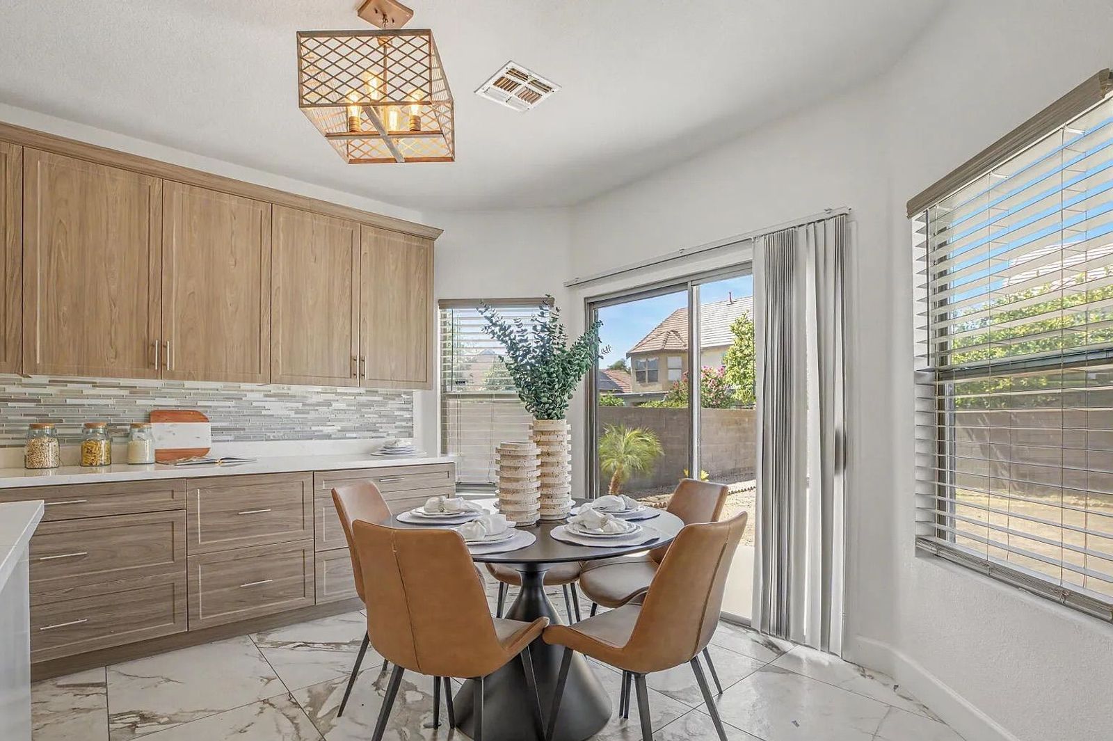 Sunny kitchen dining nook featuring a round black table with four brown leather chairs, situated next to wood-style cabinets and a sliding glass door.