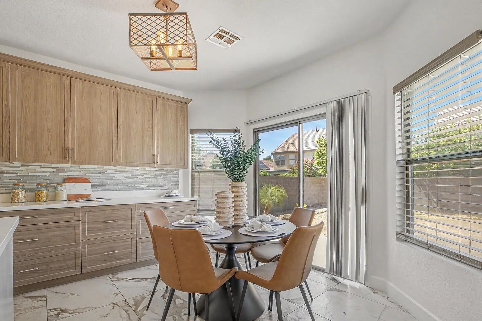 Sunny kitchen dining nook featuring a round black table with four brown leather chairs, situated next to wood-style cabinets and a sliding glass door.