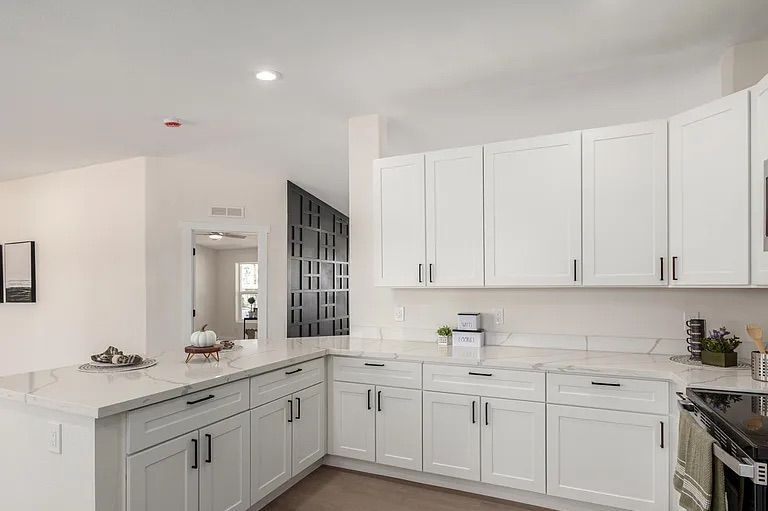 Kitchen area showcasing white cabinetry and marble-patterned quartz countertops, opening into a living space with a black geometric accent wall.