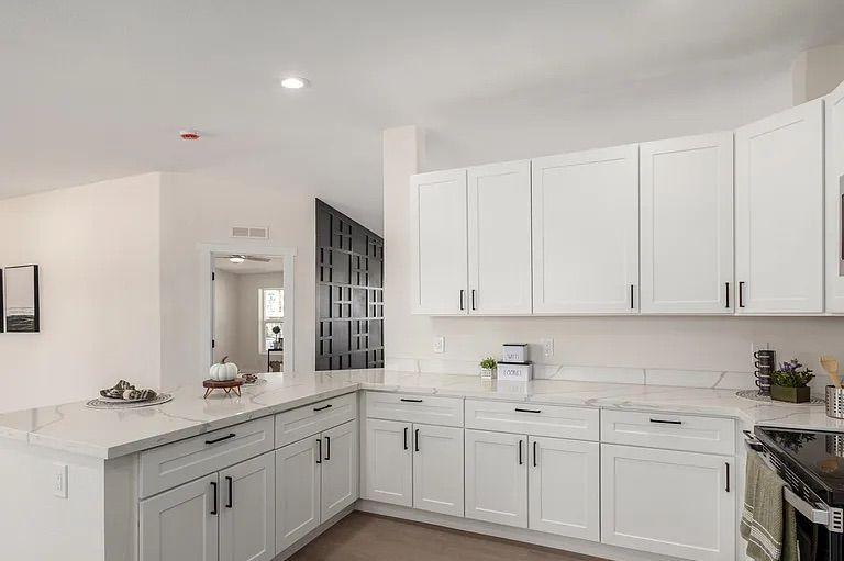 Kitchen area showcasing white cabinetry and marble-patterned quartz countertops, opening into a living space with a black geometric accent wall.